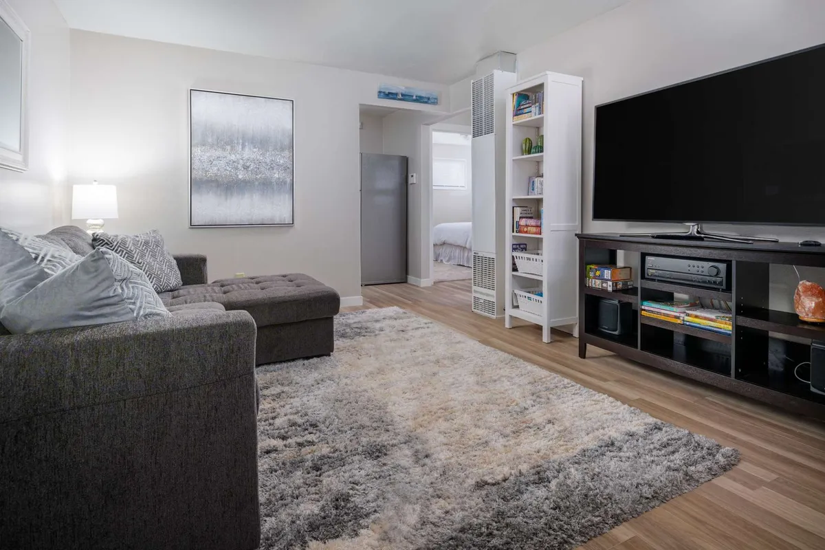 A cozy, recently renovated living room featuring a plush sofa, large television, soft area rug, and a well-stocked bookshelf, inviting guests to relax, enjoy movie nights, or curl up with a good book. The decor is warm and modern, creating an inviting atmosphere perfect for unwinding or spending time with loved ones.
