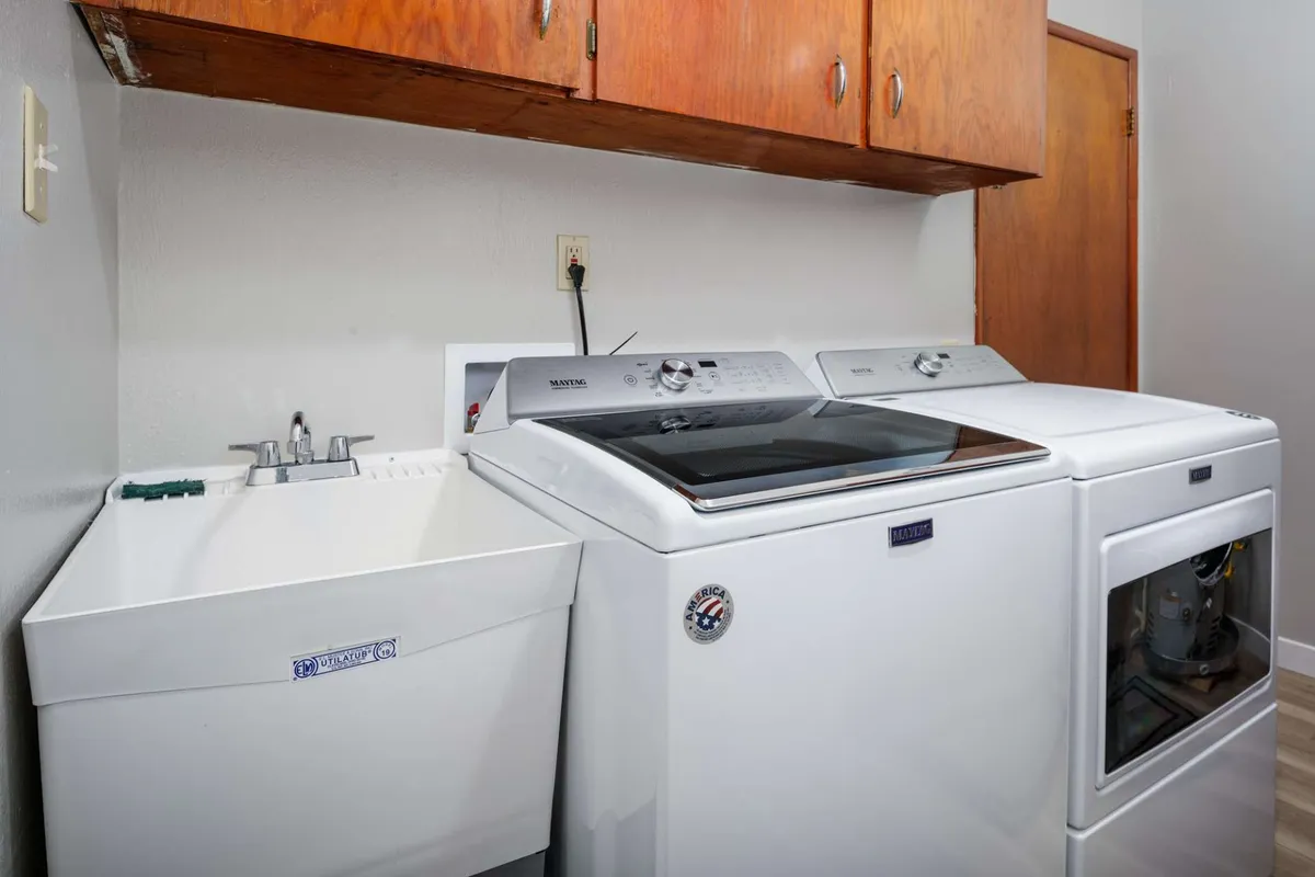 A functional laundry area outfitted with a washing machine, dryer, utility sink, and wooden cabinets. The space is organized and practical, highlighting the unit's efficiency for busy professionals.