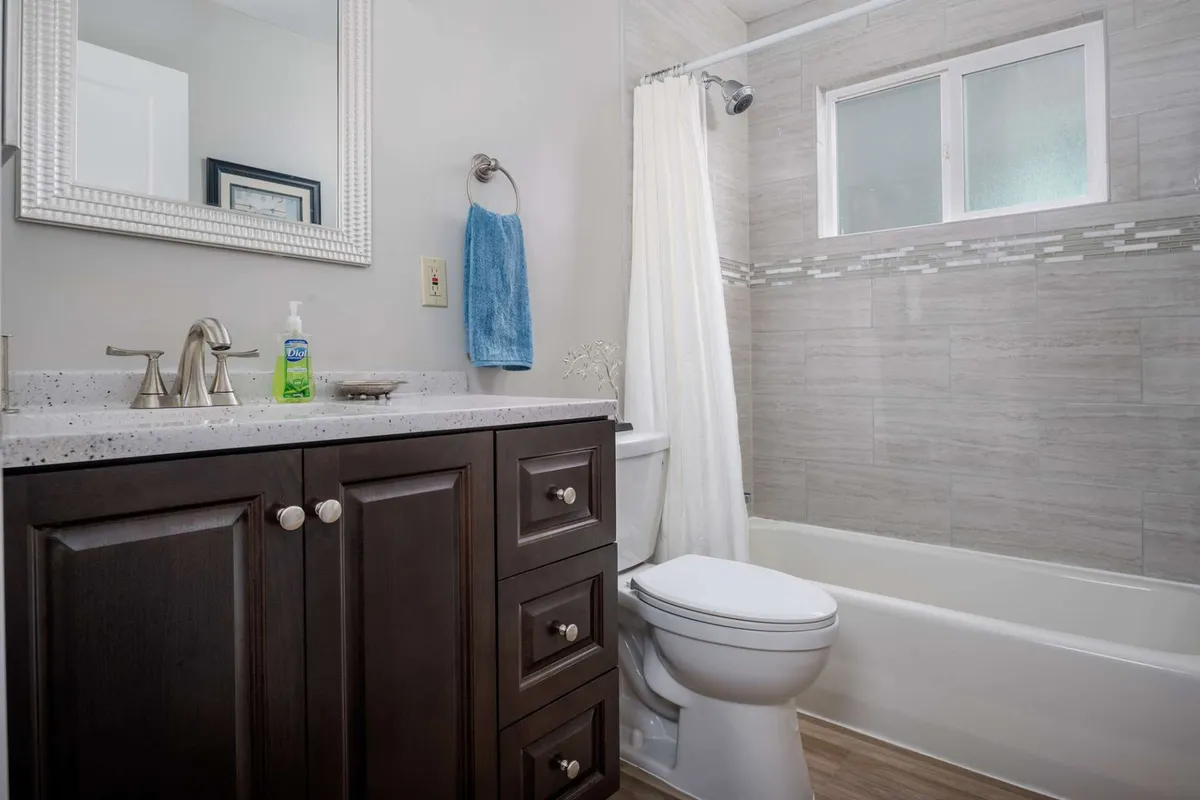 A fully remodeled bathroom with a modern vanity featuring dark cabinetry, a spacious mirror, and a bathtub partially concealed by a shower curtain. The space is well lit and exudes a crisp, spa-like ambiance perfect for unwinding after a busy day.