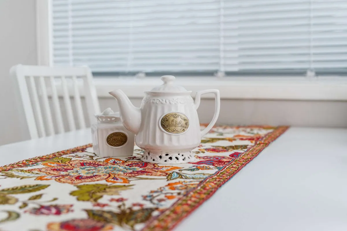 A warmly lit dining area set with a teapot, sugar bowl, and an inviting table runner, suggesting a cozy spot for group gatherings or casual conversation. The overall ambiance is welcoming, with hints of afternoon light filtering in, hinting at a space where friends might gather after a day exploring.