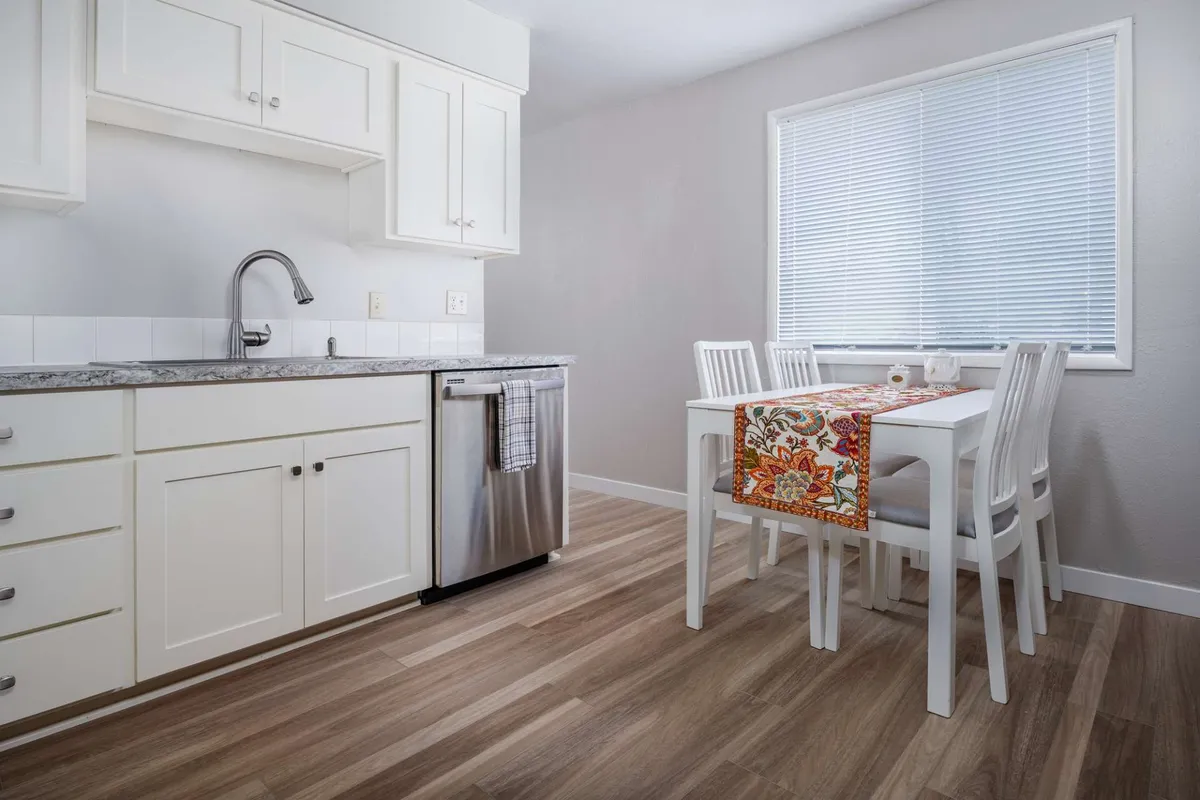 A view of a kitchen with ample cabinetry and a kitchen sink, transitioning seamlessly to an adjacent dining table set with a decorative table runner. The scene evokes warmth and social connection, suitable for dining or sharing stories.