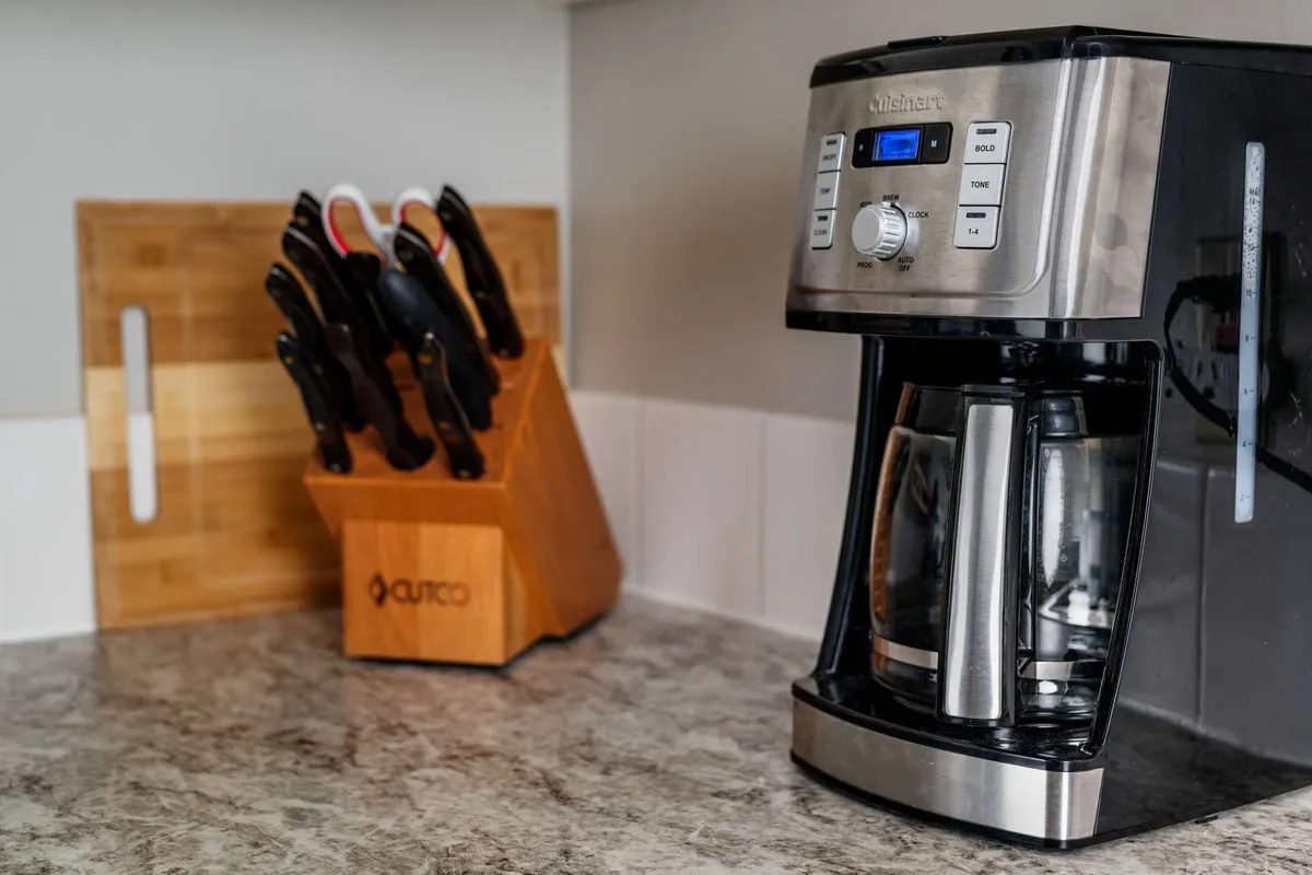 Close-up of a countertop with a coffee maker, knife block, and cutting board, suggesting readiness for meal prep or enjoying a quiet morning coffee.